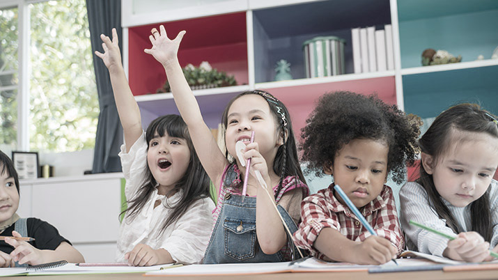 Smiling children in classroom with hands up eager to answer 